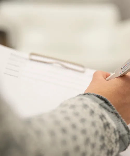 Hand hält einen Stift über einem Klemmbrett mit Papier, bereit zum Schreiben oder Ausfüllen eines Formulars.