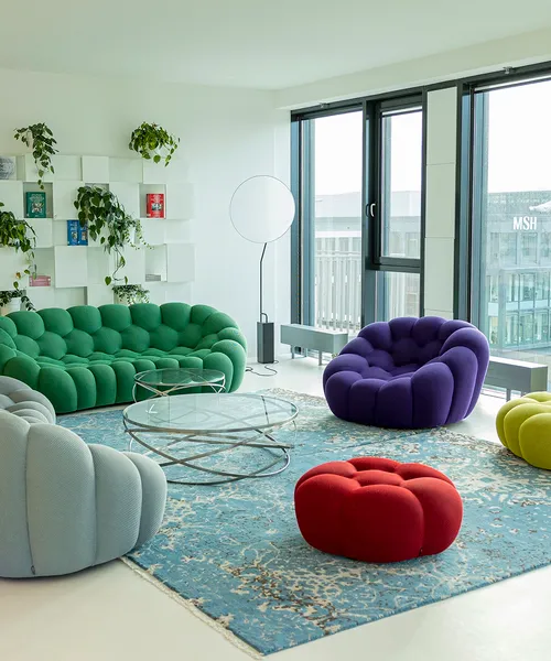 Moderner Aufenthaltsraum mit bunten Designersofas, Glas­tischen und großen Fenstern, durch die Tageslicht einfällt – eine gemütliche und offene Atmosphäre.