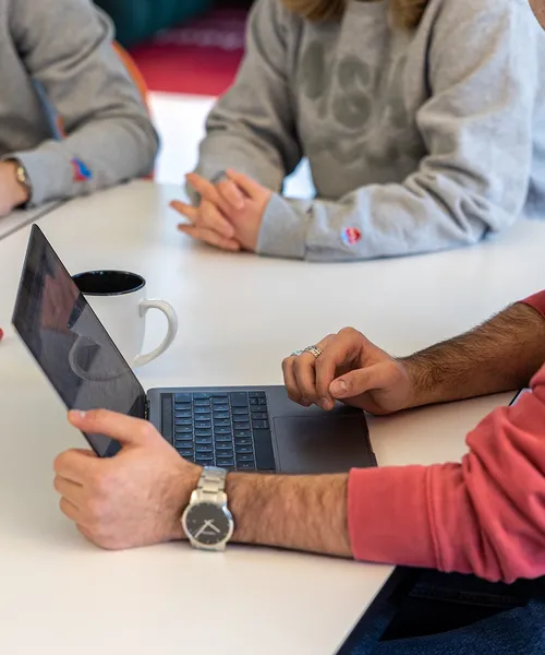 Studierende arbeiten gemeinsam an einem Tisch mit Laptop, Tasse, Stiften und einem Anatomiebuch.