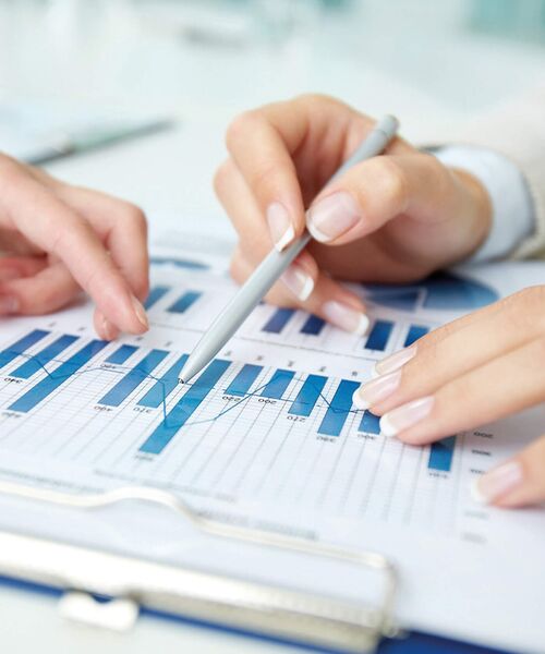 Zwei Hände zeigen mit Stiften auf ein Blatt mit blauen Balkendiagrammen und Datenanalysen auf einem Klemmbrett.