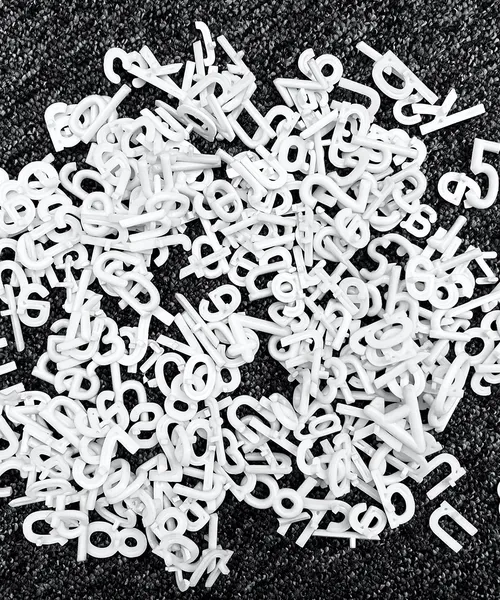 Haufen weißer Buchstaben aus Kunststoff liegen verstreut auf dunklem Untergrund.