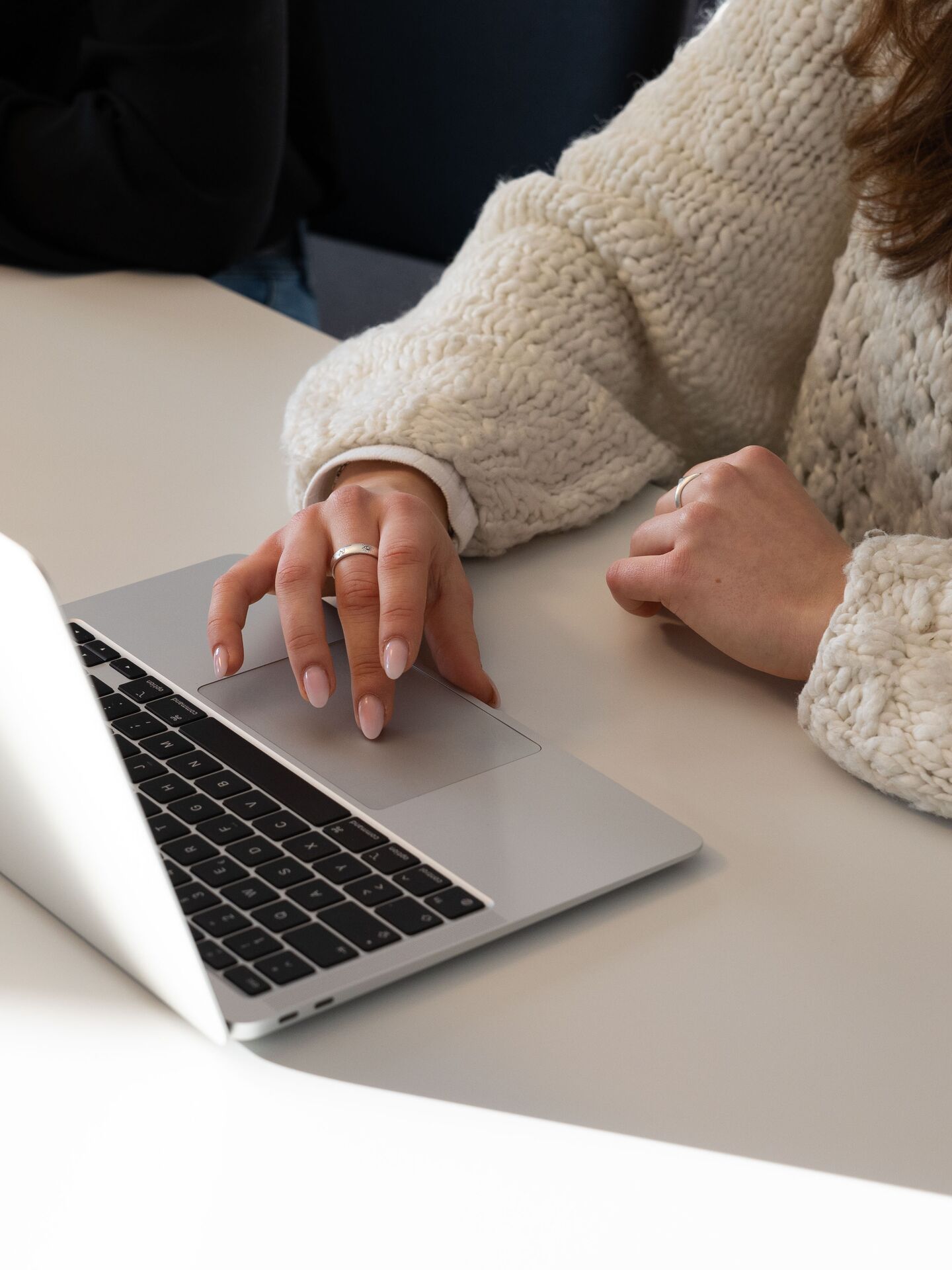 Person arbeitet an einem Laptop in heller Umgebung, Fokus auf den Händen und der Tätigkeit am Computer.