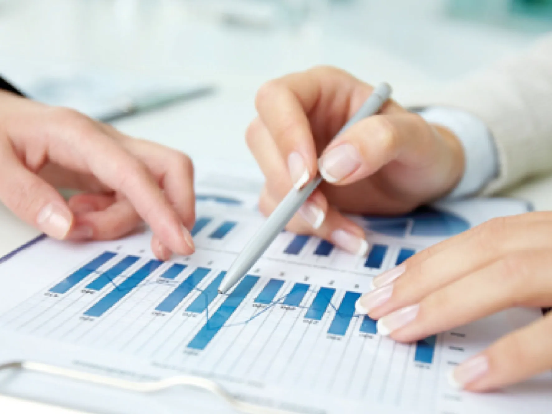 Zwei Personen analysieren ein Diagramm mit blauen Balken und Linien auf einem Dokument, Fokus auf Hände und Stift.