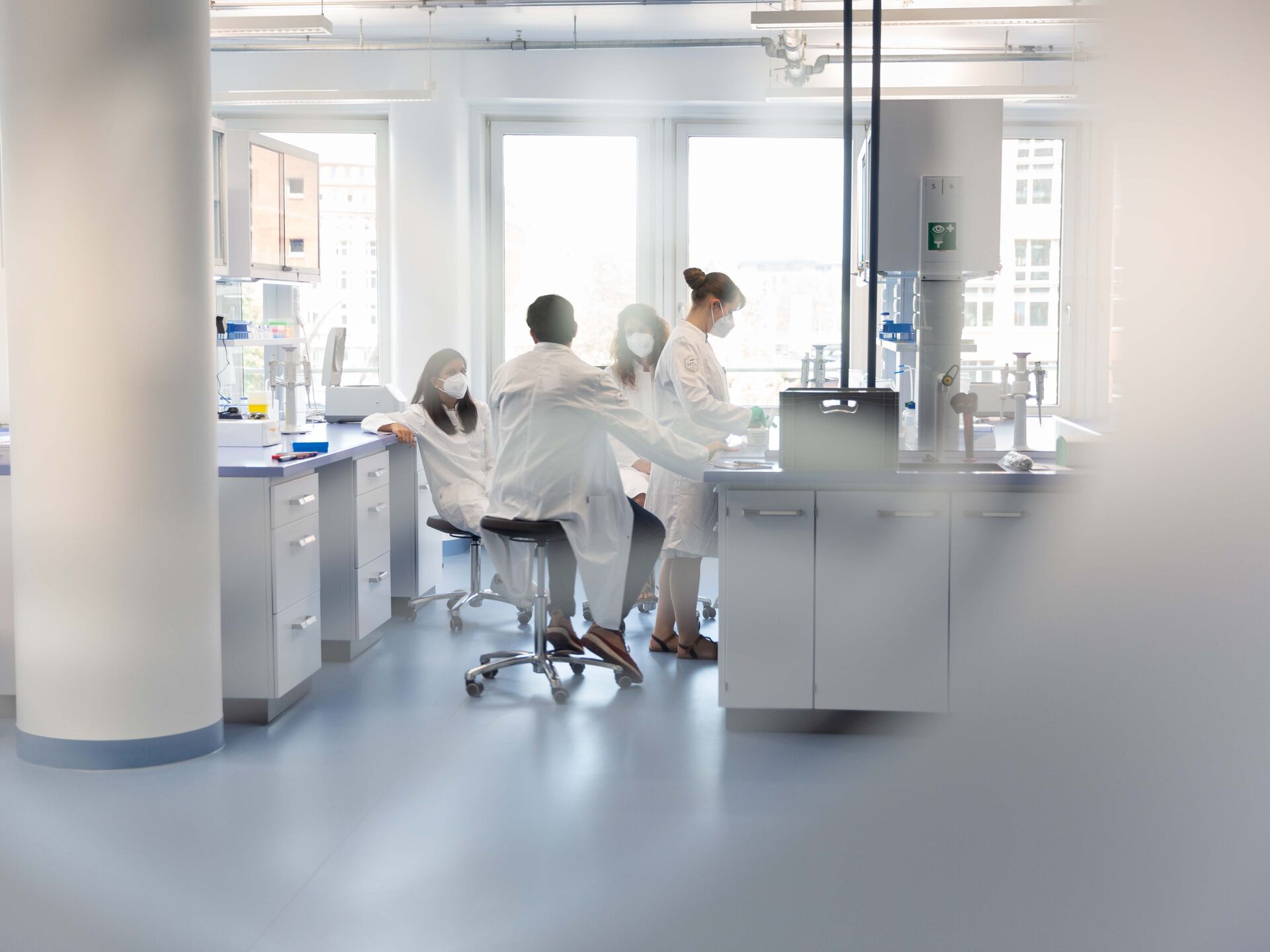 Gruppe von Labormitarbeitenden in Schutzkleidung arbeitet gemeinsam in einem hellen Forschungslabor.