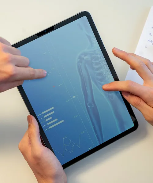 Zwei Hände bedienen ein Tablet, auf dem medizinische Daten und ein Röntgenbild angezeigt werden.