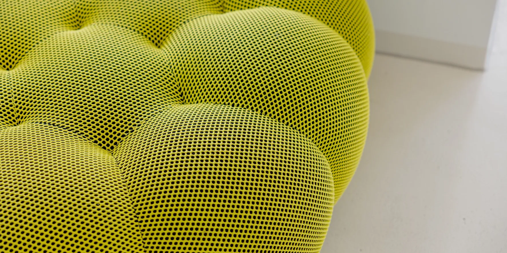 Nahaufnahme einer gepolsterten gelben Sitzfläche mit strukturierter Netzoberfläche.
