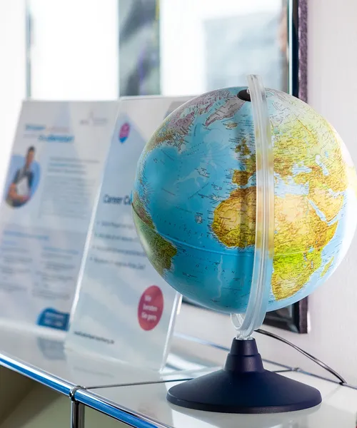 Globus mit sichtbarem Afrika und Europa steht vor einer unscharfen Infotafel an einer weißen Wand.