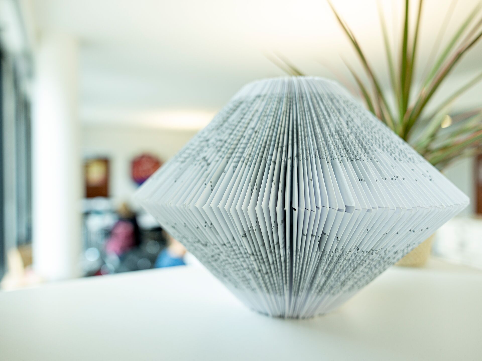 Kunstvoll gefaltetes Buch in Diamantform steht als Dekoration auf einer weißen Fläche.