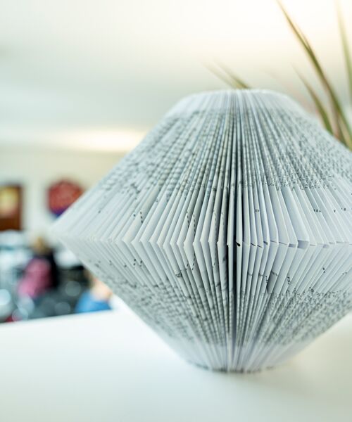 Kunstvoll gefaltetes Buch in Diamantform steht als Dekoration auf einer weißen Fläche.