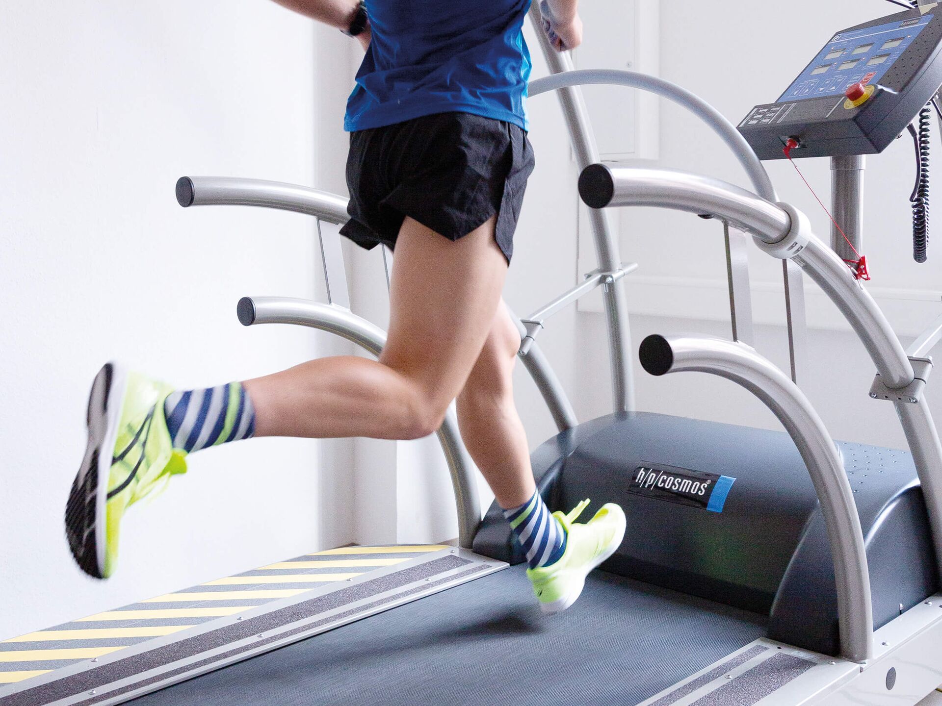 Person läuft in Sportsachen auf einem Laufband, Fokus auf den Beinen und Laufschuhen.