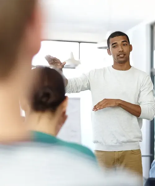 Ein junger Mann hält einen Vortrag vor einer kleinen Gruppe und gestikuliert mit den Händen, um etwas zu erklären.