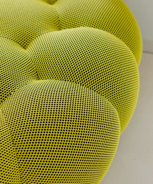 Nahaufnahme einer gepolsterten gelben Sitzfläche mit strukturierter Netzoberfläche.