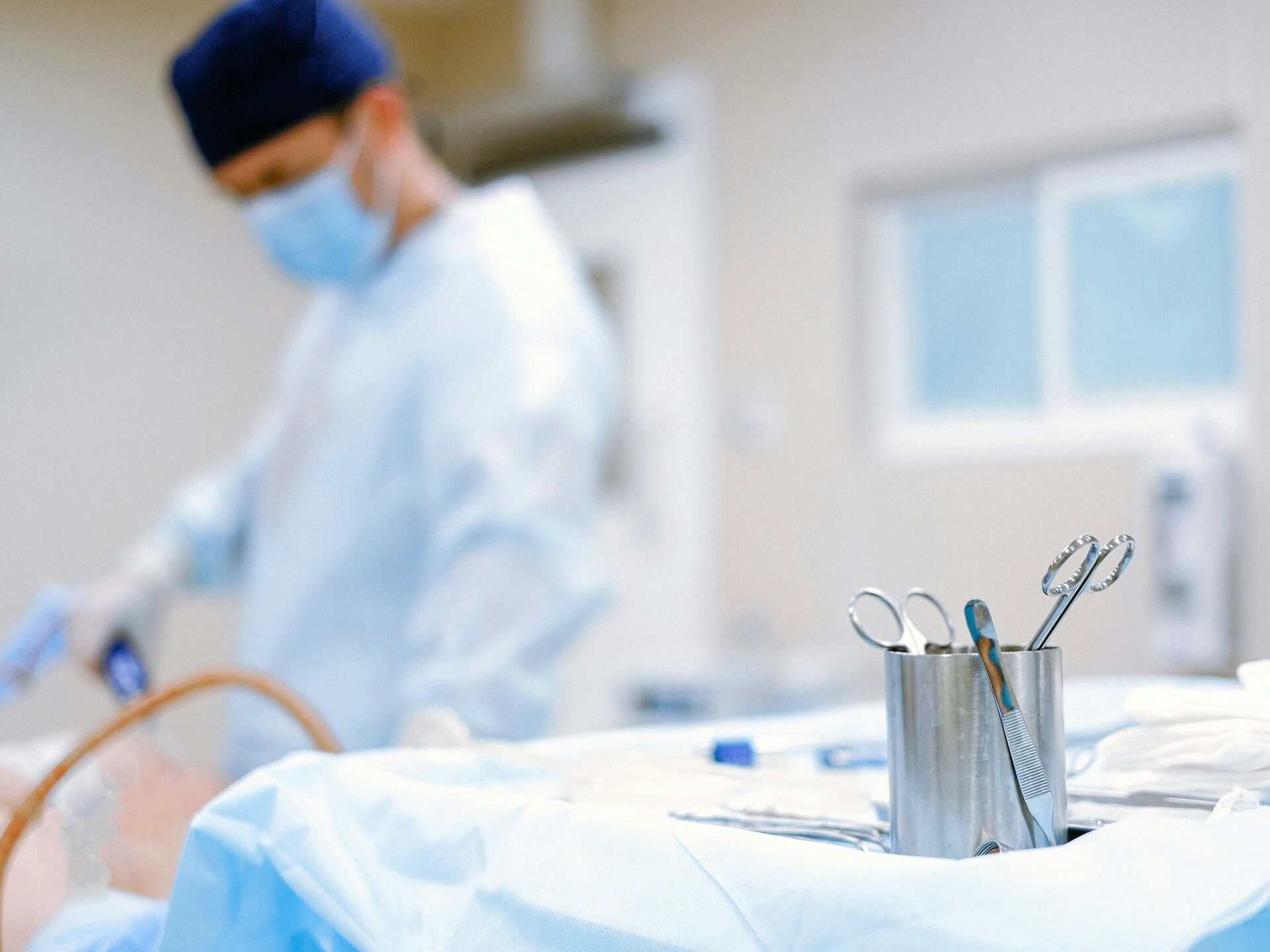 Sterile Operationsumgebung mit chirurgischen Instrumenten im Vordergrund und einer Person im OP-Kittel und Mundschutz im Hintergrund.