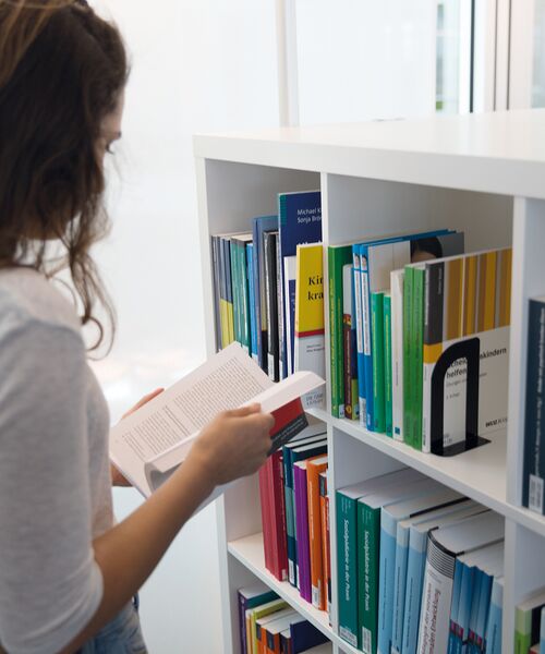 Frau steht vor einem Bücherregal und liest in einem Buch.