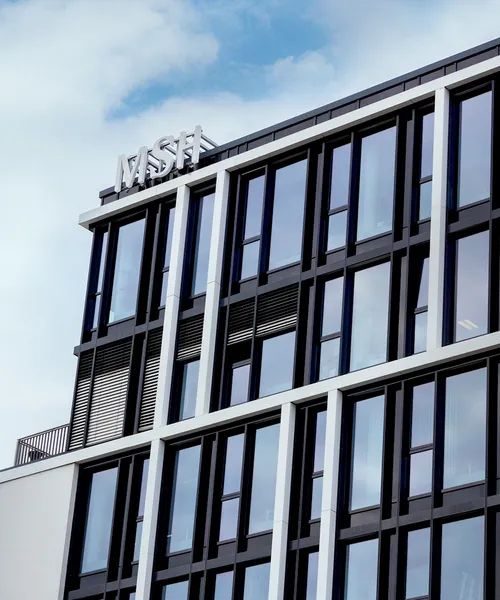 Fassade eines modernen Bürogebäudes mit großen Glasfenstern und klaren Linien vor teils bewölktem Himmel.