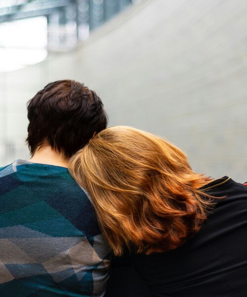 Zwei Personen sitzen nebeneinander, eine lehnt den Kopf tröstend auf die Schulter der anderen – Symbol für Nähe, Vertrauen und emotionale Unterstützung.