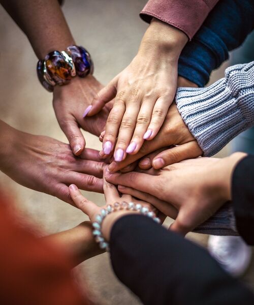Mehrere Hände liegen übereinander als Symbol für Zusammenhalt und Teamgeist.