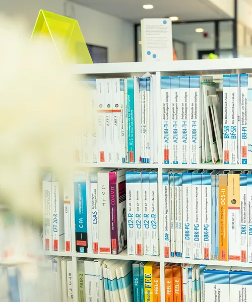 Bücherregal mit zahlreichen Fachbüchern und Testmanualen, überwiegend in Weiß- und Blautönen gehalten.