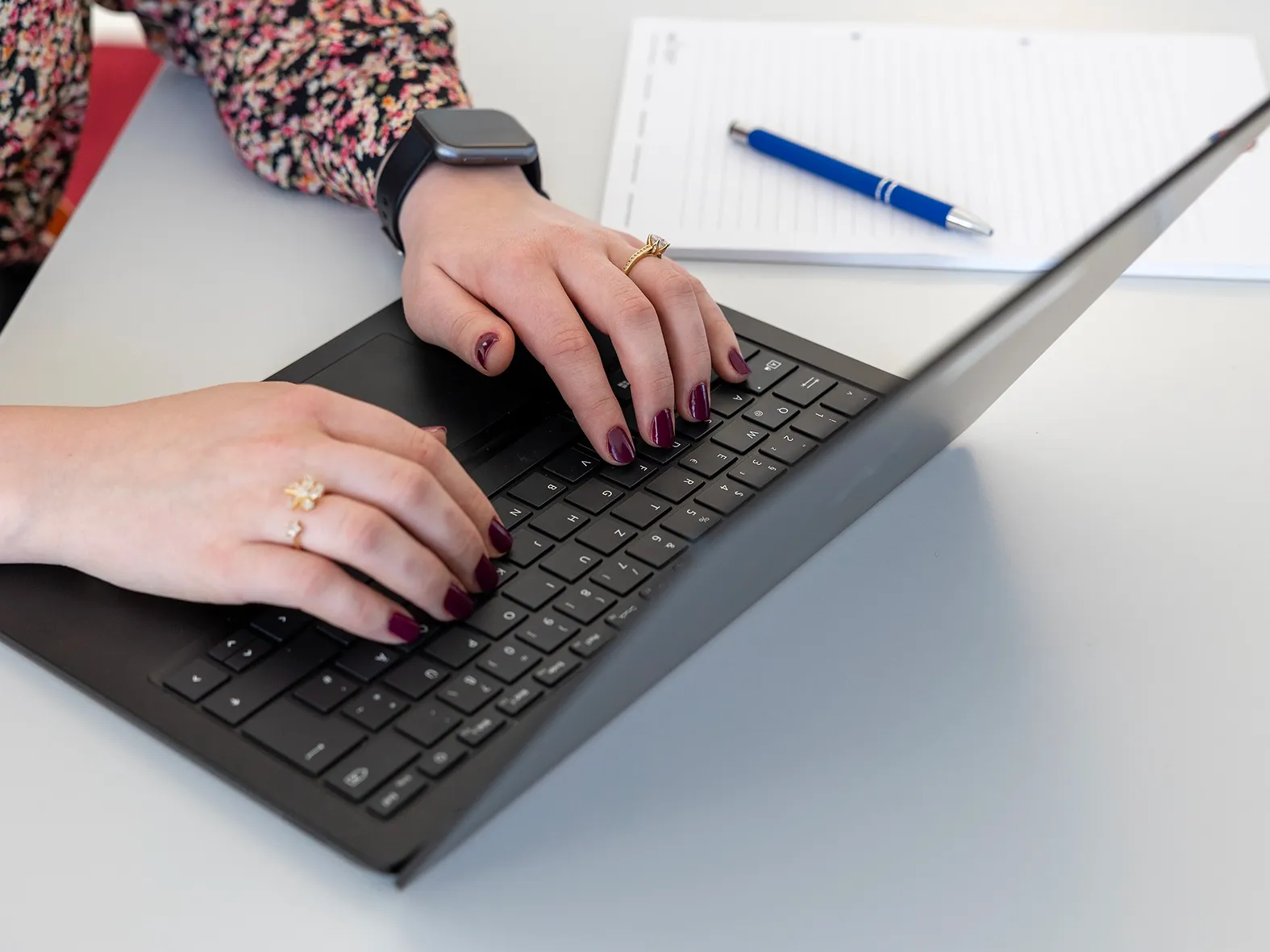 Nahaufnahme von Händen mit dunkel lackierten Nägeln, die auf einer Laptop-Tastatur tippen.