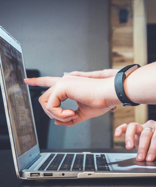 Zwei Personen arbeiten gemeinsam an einem Laptop, eine zeigt auf den Bildschirm.