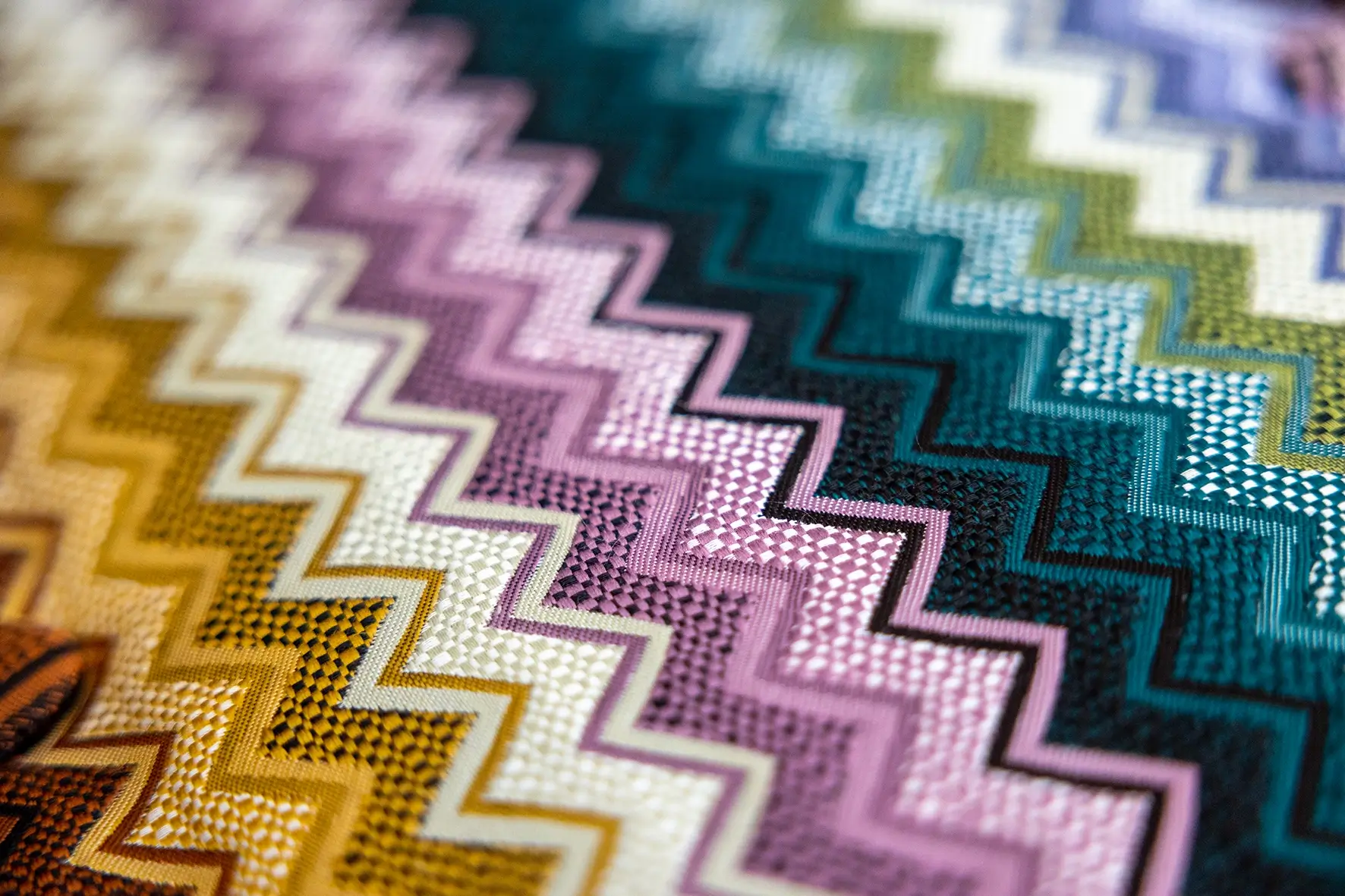 Nahaufnahme eines bunten Stoffmusters mit Zickzack-Design in verschiedenen Farben und Strukturen.