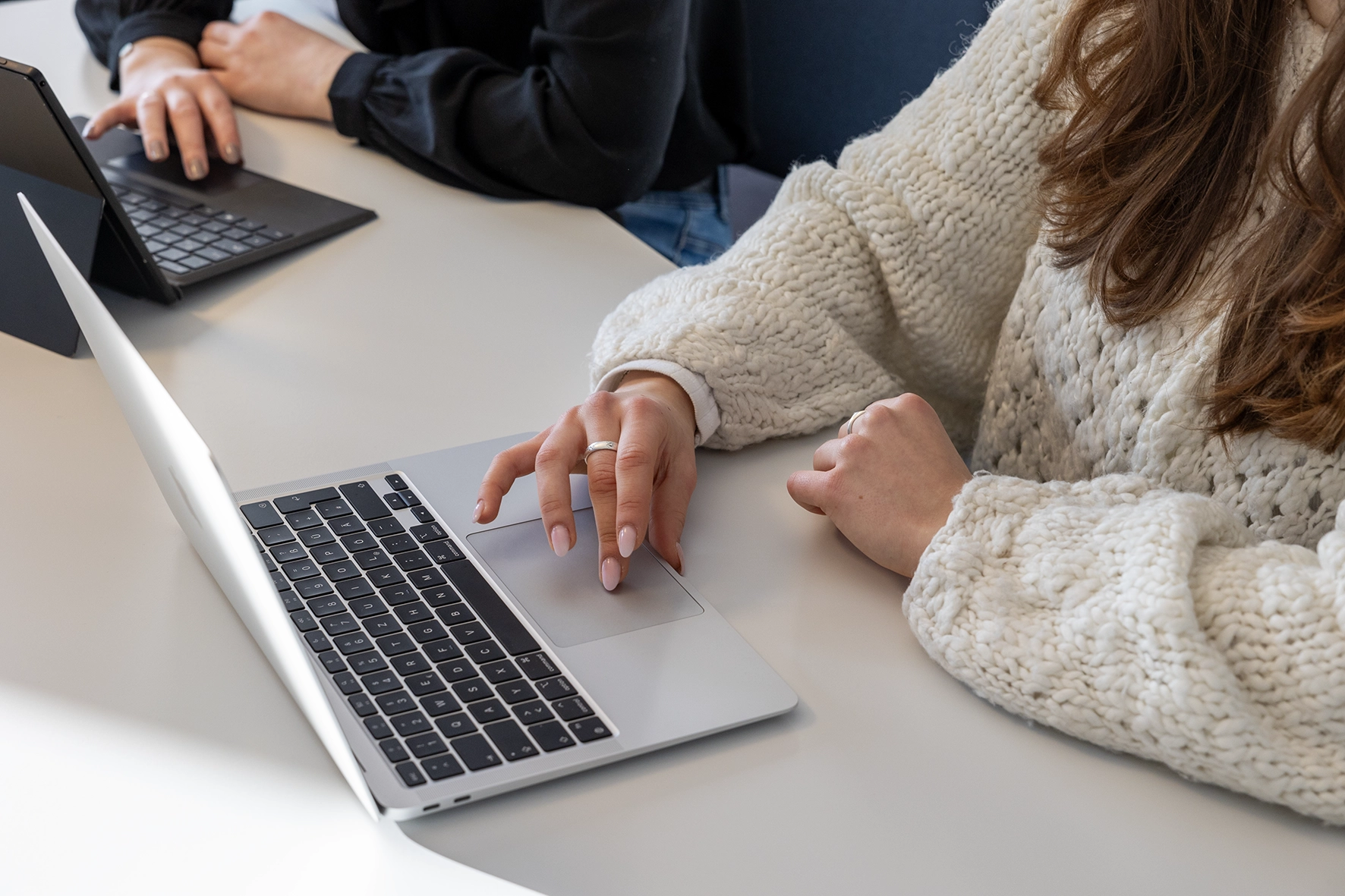 Nahaufnahme einer Person in heller Strickkleidung, die an einem Laptop arbeitet.