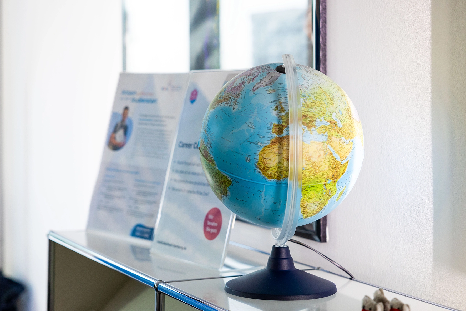 Globus mit sichtbarem Afrika und Europa steht vor einer unscharfen Infotafel an einer weißen Wand.